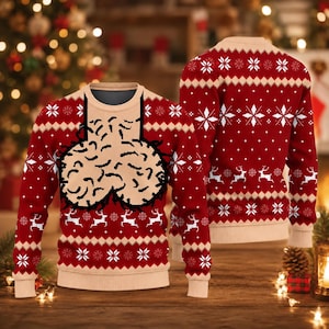 May include: A red long-sleeve jumper featuring a beige chest panel with a black graphic illustration of testicles. The jumper is decorated with a repeating white pattern of snowflakes and reindeer across the sleeves and the lower body section.