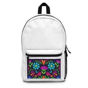 Puede incluir: Una mochila blanca con un asa superior negra y un bolsillo frontal con cremallera negra. El bolsillo frontal muestra un patrón floral simétrico y vibrante sobre un fondo oscuro, que incluye flores azules, rosas y naranjas y un corazón.