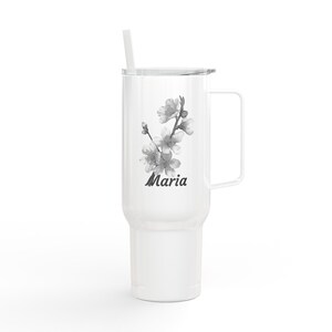 Op de afbeelding: Een witte roestvrijstalen beker met een handvat, een deksel en een rietje. De voorzijde is voorzien van een zwart-witte illustratie van een bloeiende tak en de naam Maria in een donker scriptlettertype in het midden van de beker.