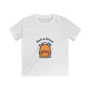 Puede incluir: Una camiseta blanca de manga corta con un gráfico central de una mochila naranja con bolsillo frontal, que contiene lápices y un libro. Sobre la mochila, el texto Back to School está impreso en una fuente azul oscuro curvada con pequeñas estrellas de colores.