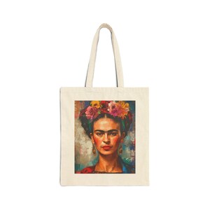 Puede incluir: Un bolso de tela color crema con un estampado rectangular de un retrato de Frida Kahlo. El retrato muestra a una persona con cabello oscuro adornado con una corona floral vibrante, usando pendientes dorados sobre un fondo texturizado.