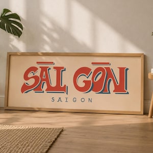 以下が含まれることがあります： ライトベージュの背景に、赤と青の大きなレトロ調の文字で「SAI GON」と書かれ、その下に小さな黒い大文字で「SAIGON」と記された、長方形の額入りウォールアート作品。