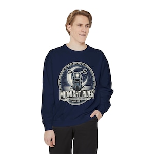 Puede incluir: Una sudadera azul marino de manga larga con un gráfico circular en el pecho. El diseño muestra una motocicleta frente a una luna creciente, rodeada por un borde de cadena, con el texto "MIDNIGHT RIDER MOTORCYCLE CULTURE EST. 1978."