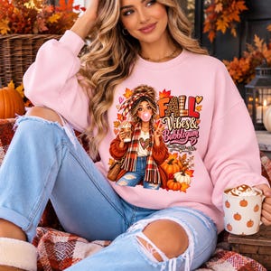 Puede incluir: Una sudadera de cuello redondo rosa claro con una ilustración gráfica de una persona con un moño haciendo una burbuja, con una bufanda de cuadros y sosteniendo un café, con el texto "FALL Vibes & Bubblegum SWEET SASSY COZY".