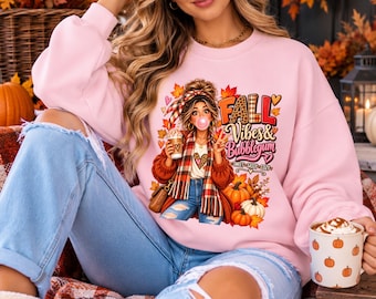 Peut inclure: Un sweat-shirt à col rond rose clair avec une illustration graphique d'une personne en chignon faisant une bulle, portant une écharpe à carreaux et tenant un café, avec le texte "FALL Vibes & Bubblegum SWEET SASSY COZY".