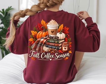 Peut inclure: Un sweat-shirt bordeaux à manches longues avec un motif au dos représentant une tasse de café, des citrouilles, une écharpe à carreaux, une pile de livres et une bougie. Le texte "Fall Coffee Season" est imprimé sous l'illustration automnale.