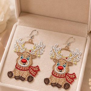 May include: A pair of embroidered reindeer earrings featuring a tan deer with a bright red nose, wearing a red and white striped scarf. The reindeer antlers are white with gold-colored string lights attached, and each earring has a silver-toned hook.