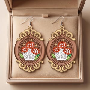 Può includere: Un paio di orecchini pendenti ovali con un intricato ricamo di tre funghi con cappelli arancioni e gambi bianchi. Il design è inserito in una cornice marrone con decorazioni dorate a volute e ganci per orecchini color argento.