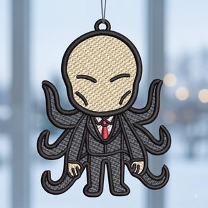 May include: A hanging ornament featuring an embroidered character with a pale, round head, closed eyes, and a dark suit with a red tie. The figure has multiple black tentacles extending from its sides and a small loop at the top for hanging.
