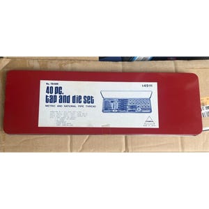 Könnte beinhalten: Ein rechteckiger roter Metallkoffer für ein 40-teiliges Gewindeschneidwerkzeug-Set. Das weiße Etikett auf der Vorderseite zeigt den Text '40 pc. tap and die set', 'Metric and National Pipe Thread', 'Cobra' sowie eine Strichzeichnung des Inhalts.