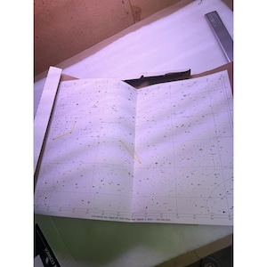 Può includere: Una mappa stellare bianca stampata su carta con una griglia di punti neri che rappresentano stelle e costellazioni. Due linee gialle collegano specifici ammassi stellari. Il margine inferiore include il testo International Star Registry 34253 Wilson Road Ingleside, IL 60041 1-800-282-3333.