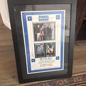 May include: A framed poster for The Blue Aces featuring photographs of the band members, including Johnny Dyer and Mark the Harp. The poster includes text detailing a performance on December 4, 2004, at the Manchester Grand Hyatt Redfield's Lounge.