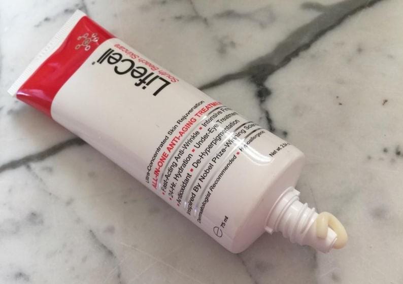May include: A white and red squeeze tube of LifeCell All-In-One Anti-Aging Treatment skincare cream. The tube features black text listing benefits like anti-wrinkle and hydration, with a small amount of beige cream dispensed from the nozzle, 75 ml.