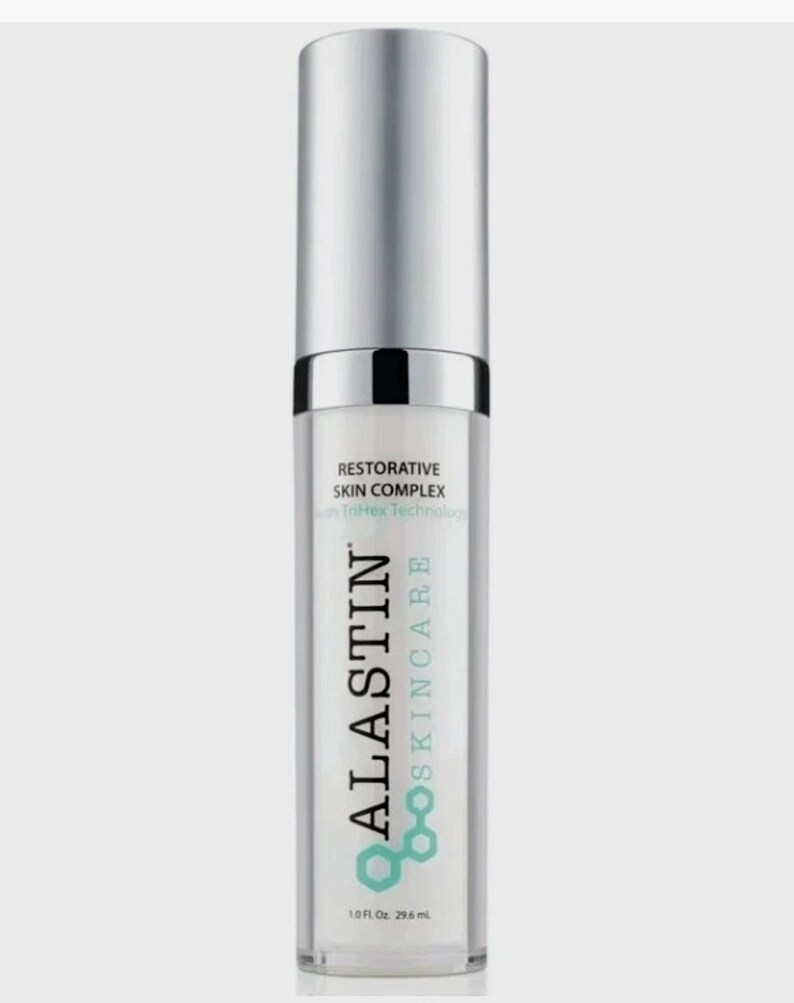 May include: A cylindrical skincare bottle with a silver cap and a clear body. The label reads ALASTIN SKINCARE, RESTORATIVE SKIN COMPLEX, with TriHex Technology, and 1.0 Fl. Oz. 29.6 mL. The design features a teal hexagonal logo graphic.