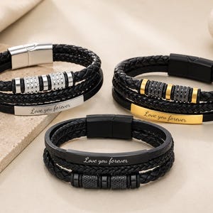 May include: Three multi-strand bracelets featuring braided black leather cords and smooth leather bands. Each bracelet includes a metal plate engraved with the text Love you forever and decorative cylindrical beads with embedded crystals.