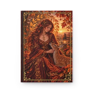 Puede incluir: Un diario de tapa dura con la ilustración de una persona de largo cabello caoba con un vestido rojo oscuro, tocando suavemente a un cervatillo. La escena se sitúa en un bosque otoñal con hojas naranjas, atardecer y un borde dorado.