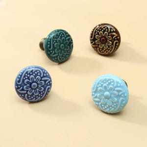 Puede incluir: Cuatro pomos redondos de cerámica para armarios con patrones florales en relieve y detalles de puntos. El conjunto incluye un pomo de color verde azulado oscuro, marrón oscuro, azul profundo y azul cielo claro, cada uno con una base de tornillo.