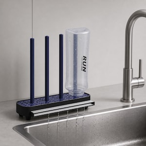 Puede incluir: Un escurridor de botellas de plástico negro y azul con tres postes verticales y una base perforada. Una botella de agua de plástico transparente con la palabra RUN impresa en negro está invertida sobre un poste, goteando agua hacia el fregadero.