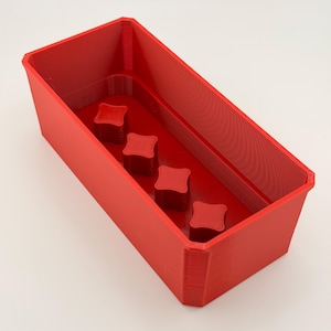 May include: A bright red rectangular container with four square, raised, decorative elements inside. The container has a slightly textured surface and is likely 3D printed. The design is simple and modern, suitable for various organizational purposes.