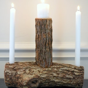 May include: A rustic wooden candle holder with three candle slots. The holder is made from a natural log with bark still attached. Two tall white candles are in the slots on either side, and a shorter white candle is in the center slot.