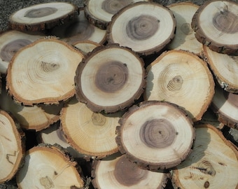 May include: A pile of round wooden slices, each with a unique grain pattern. The slices are various shades of brown and beige, with some having a darker brown center. The wood is smooth and polished, and the edges are slightly rough.