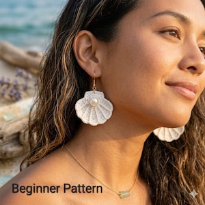 Könnte beinhalten: Ein Paar cremeweiße Häkel-Ohrringe in Muschelform mit einer zentralen weißen Perle auf jedem Stück. Die Ohrringe hängen an goldfarbenen Metallhaken. Der Text "Beginner Pattern" ist in der unteren linken Ecke des Bildes zu sehen.