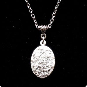 May include: Silver-toned oval pendant necklace featuring a detailed relief scene of a church and figures. The pendant hangs from a delicate chain. The background is black, highlighting the necklace's intricate design and metallic sheen.