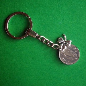 Könnte beinhalten: Silberner Schlüsselanhänger mit einem Kleeblatt-Anhänger und einer irischen Münze aus dem Jahr 1962 mit einer Harfe. Die Münze ist mit einer silbernen Kette am Anhänger befestigt.