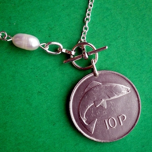 May include: A silver necklace with a silver toggle clasp and a silver charm featuring a fish and the text "10P". The necklace also has a white pearl bead.