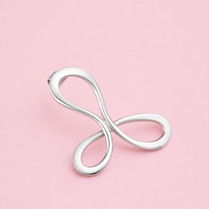 May include: A polished silver-tone metal brooch featuring a continuous, fluid, and abstract looped design. The piece consists of three interconnected, rounded, and smooth-surfaced loops that form a symmetrical, organic shape with a reflective finish.