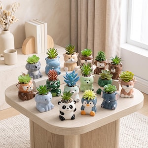 May include: A collection of small ceramic animal-shaped planters, each containing a faux succulent. The figures include a panda, penguin, elephant, koala, hippo, cat, bear, deer, and other creatures, featuring painted faces and smooth, glossy finishes.