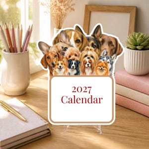 May include: A 2027 calendar featuring a collage of various dog breeds including a dachshund, corgi, beagle, and husky. The calendar has a white rectangular base with the text 2027 Calendar printed in dark red letters on the front surface.