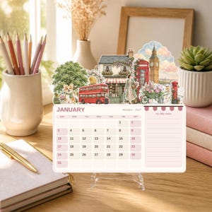 May include: A 2027 desk calendar for January featuring a die-cut illustration of a London street scene with a red double-decker bus, Big Ben, a corgi, and a person. The calendar grid includes dates for the month and a section for notes.