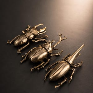 May include: Three metallic beetle figurines with a bronze finish. The first beetle features large, curved mandibles. The second beetle has a prominent horn on its head. The third beetle displays a long, singular horn extending from its thorax.