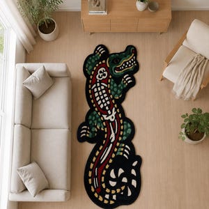 May include: A large, irregularly shaped area rug featuring a stylised crocodile design. The rug is primarily black with a central red section, white skeletal-like patterns, and green textured details on the crocodile's body and limbs.