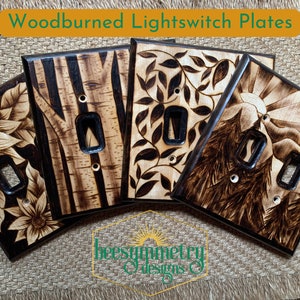 Op de afbeelding: Vier gebrandschilderde lichtschakelaarplaten met verschillende ontwerpen. De ontwerpen omvatten een ​​zonnebloem, bomen, bladeren en een berglandschap. De platen zijn allemaal van hout en hebben een donkerbruine afwerking.