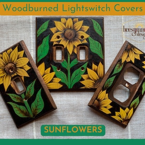 May include: Three woodburned light switch covers with a sunflower design. The covers are painted black with yellow sunflowers and green leaves. The text "beesymmetry designs" is visible in the top right corner of the image. The text "SUNFLOWERS" is visible in the bottom center of the image.