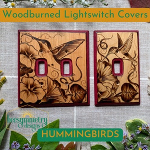 以下が含まれることがあります： ハチドリと花の模様が施された、木を焼いたライトスイッチカバー2枚。カバーは明るい色の木材で作られており、濃い赤色の縁取りがあります。「Woodburned Lightswitch Covers」と「HUMMINGBIRDS」の文字が見えます。