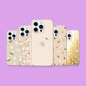 May include: Five smartphone cases arranged in a row, each featuring a unique design with bees, daisies, and floral patterns in shades of yellow, white, and beige. The cases have cutouts for camera lenses and are displayed against a solid purple background.