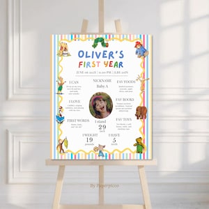 May include: A rectangular milestone poster titled OLIVER'S FIRST YEAR with colorful vertical stripes, a yellow wavy border, and illustrations of storybook characters. It features a central photo of a child, text details, and measurements.