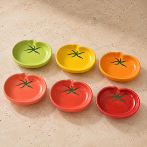 Peut inclure: Un ensemble de six petits plats en céramique en forme de tomates, chacun orné d'un motif de tige verte peinte. La collection comprend un plat vert clair, un jaune, un orange, un rouge clair, un rouge moyen et un rouge foncé.