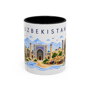 Puede incluir: Una taza de cerámica blanca con borde interior negro que presenta una ilustración colorida de la arquitectura de Uzbekistán, con cúpulas y arcos azules sobre un fondo de montañas y la palabra UZBEKISTAN impresa en azul arriba.