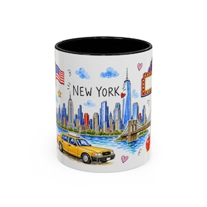 May include: A white ceramic mug with a black interior and rim, featuring a colorful watercolor illustration of the New York City skyline, a yellow taxi, the Brooklyn Bridge, and the text NEW YORK in black lettering with small red hearts.