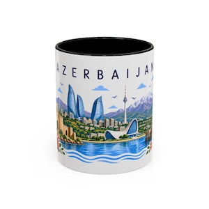 Puede incluir: Una taza de cerámica blanca con borde interior negro que presenta una ilustración colorida del horizonte de Bakú en Azerbaiyán. El diseño incluye las Flame Towers, el Centro Heydar Aliyev y montañas bajo el texto AZERBAIJAN.