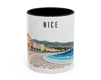 May include: A white ceramic mug with a black interior featuring a colorful illustration of the Nice coastline, including a pebble beach, palm trees, multi-colored buildings, and hills under a clear sky, with the word NICE printed in dark blue.