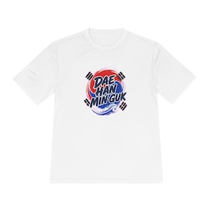 Könnte beinhalten: Ein weißes kurzärmeliges T-Shirt mit einem zentralen Grafikdesign. Die Grafik zeigt ein rot-blaues kreisförmiges Emblem mit vier schwarzen Trigrammen, überlagert mit dem Text DAE HAN MIN GUK in dunkelblauen Buchstaben und einer Wellenillustration.