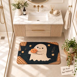 May include: A rectangular bath mat with a dark blue background featuring a central cream-colored ghost holding an orange pumpkin. The mat has brown plaid corner patches, small yellow star accents, and a safety pin graphic on the right side.