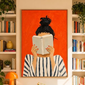 Puede incluir: Un cuadro enmarcado de una persona con un moño oscuro y una camisa de rayas azul marino y blancas, sosteniendo un libro abierto frente a su cara sobre un fondo naranja brillante. La pintura se exhibe en una pared entre dos estanterías blancas.