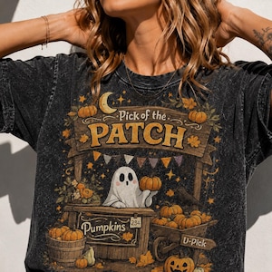Könnte beinhalten: Ein anthrazitfarbenes T-Shirt in Acid-Wash-Optik mit einer Grafik eines Geistes, der hinter einem Holzstand einen Kürbis hält. Der Text lautet Pick of the PATCH, Pumpkins und U-Pick. Das Design zeigt Kürbisse, einen Mond und Herbstblätter.