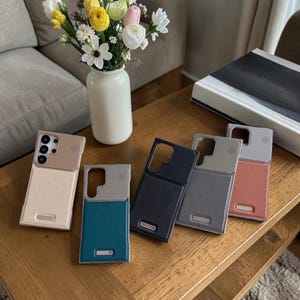 Könnte beinhalten: Fünf rechteckige Smartphone-Hüllen mit zweifarbigem Design, ausgestattet mit einem Kameraausschnitt und einem kreisförmigen magnetischen Ladebereich. Die Hüllen sind in Beige, Petrol, Schwarz, Grau und Koralle erhältlich.